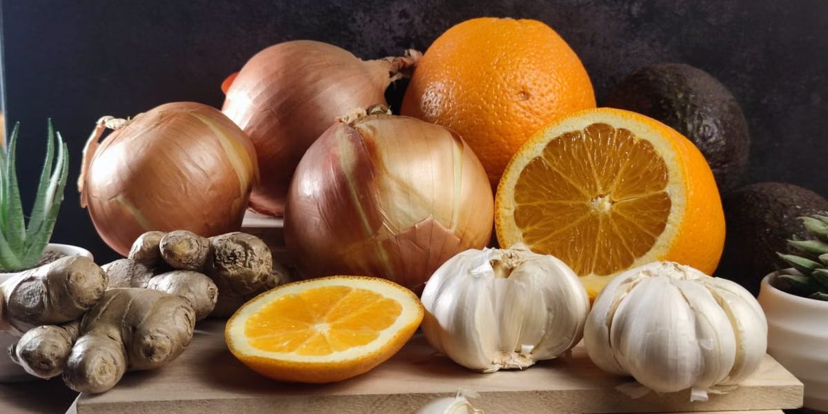 Fresh oranges, onions, garlic, and ginger arranged on a wooden board, perfect for healthy lifestyle visuals.
