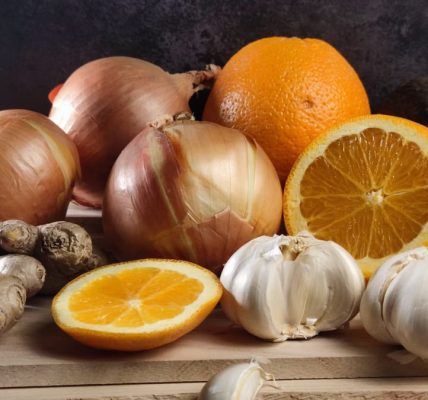 Fresh oranges, onions, garlic, and ginger arranged on a wooden board, perfect for healthy lifestyle visuals.