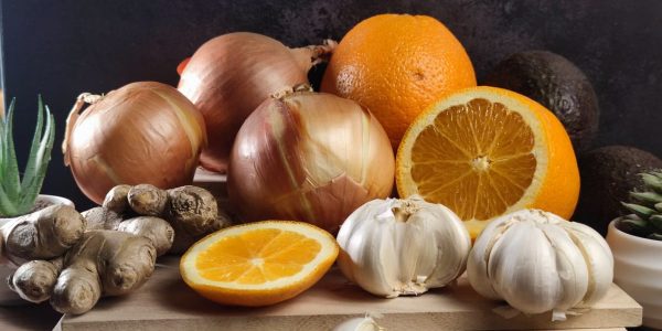 Fresh oranges, onions, garlic, and ginger arranged on a wooden board, perfect for healthy lifestyle visuals.