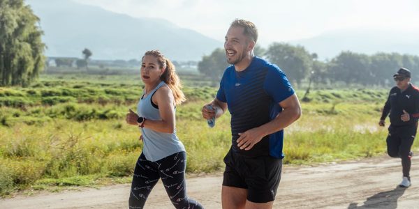 Two adults running on a rural dirt path, enjoying a sunny day outdoors.